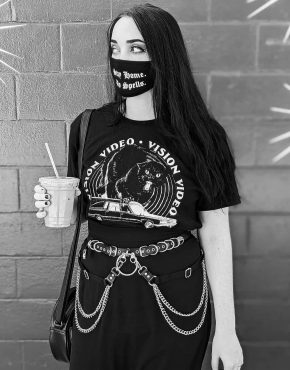 gothic girl in a mask and chain belt harness holds a drink