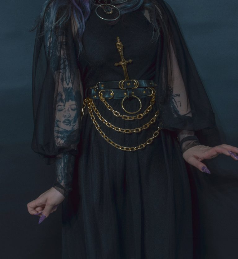 tattooed goth girl in black dress wearing golden hardware belt